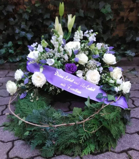 Trauerkranz mit Konifere gewickelt und dekorativ hoch gesteckt mit Rosen, Muscari, Wachsblume, Campanula und Eustoma.